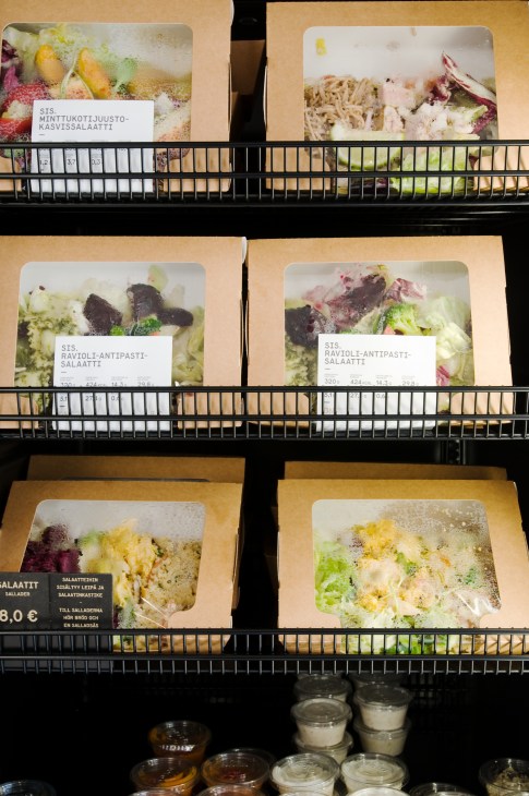 Display shelf of Sis ready-made meals in paper containers with white labels showing Finnish names and prices.