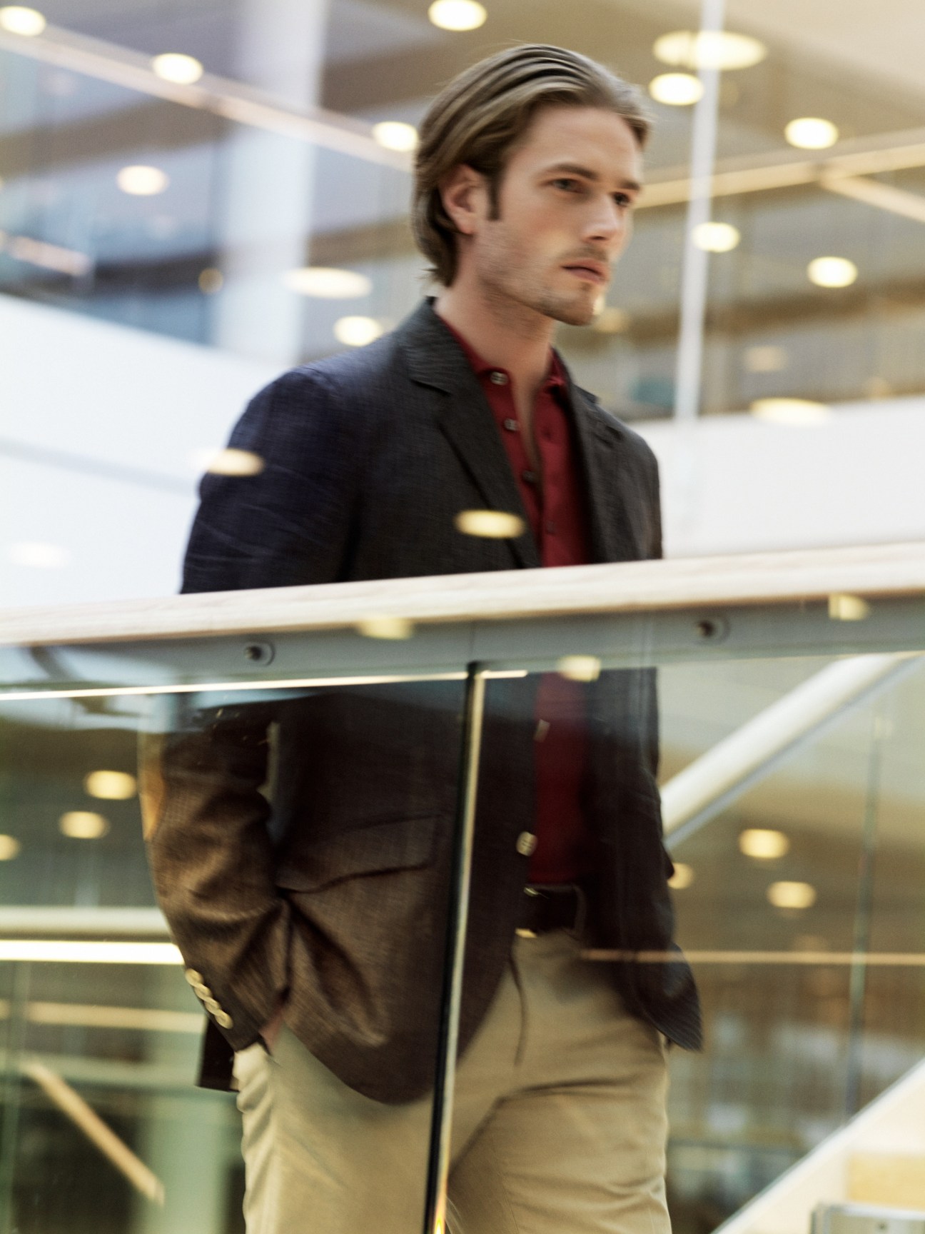 Male model wearing linen jacket, polo shirt, cotton trousers, belt and loafers in modern office foyer.