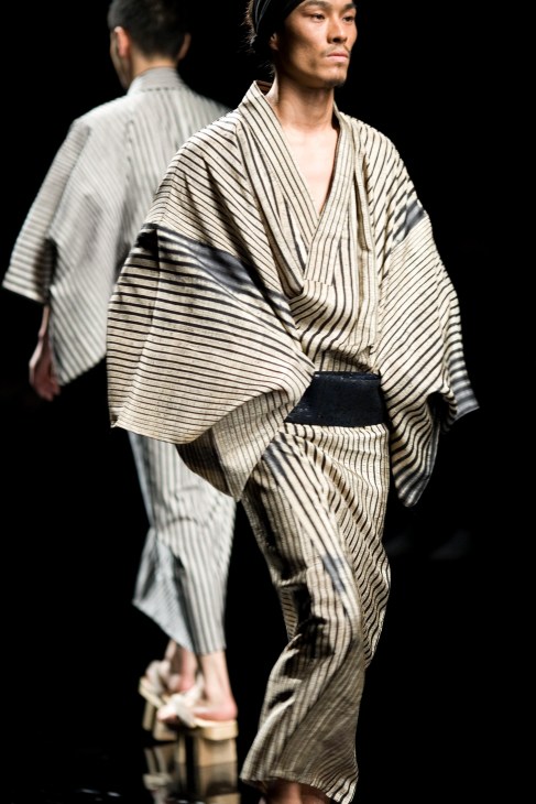 Model wearing black and white striped silk yukata with deerskin obi on catwalk.