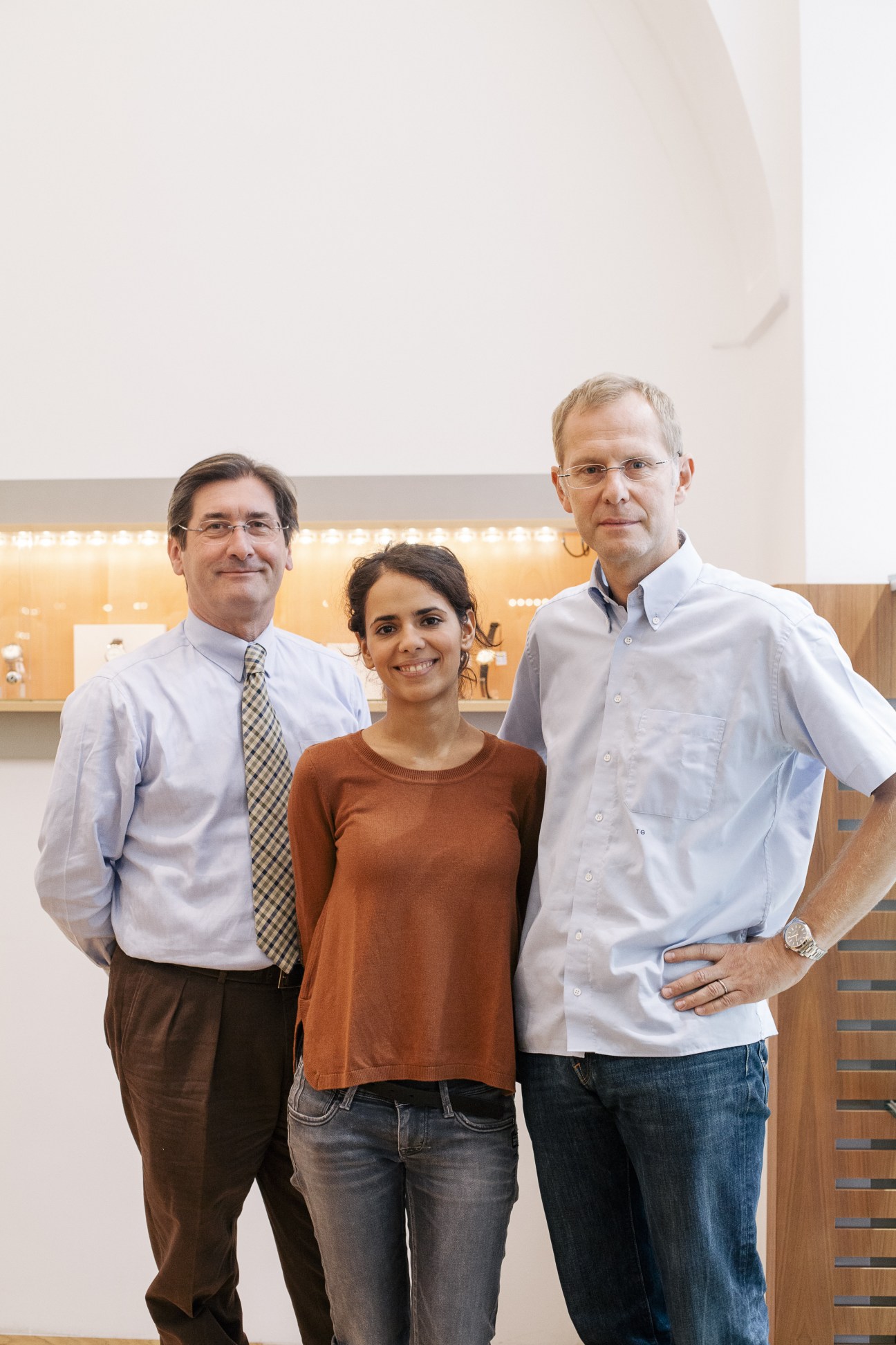 Three people posing together in a modern retail space with illuminated shelving behind them.