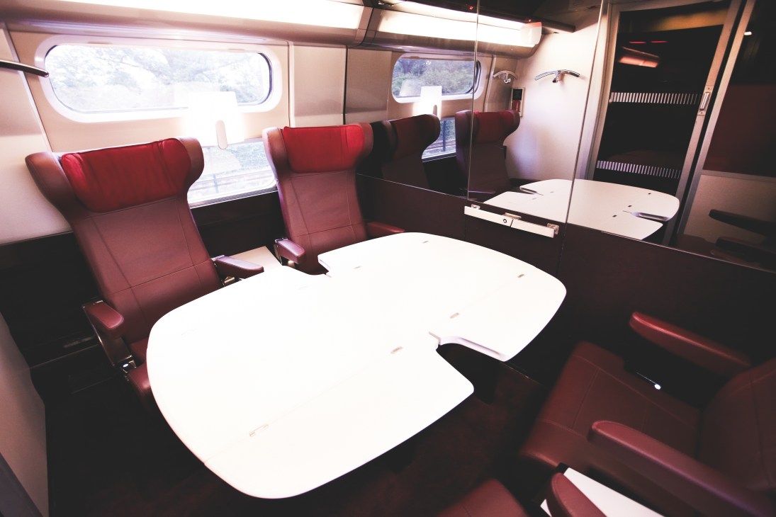 Interior of Thalys train meeting room with red seats, white tables, and windows showing landscape.