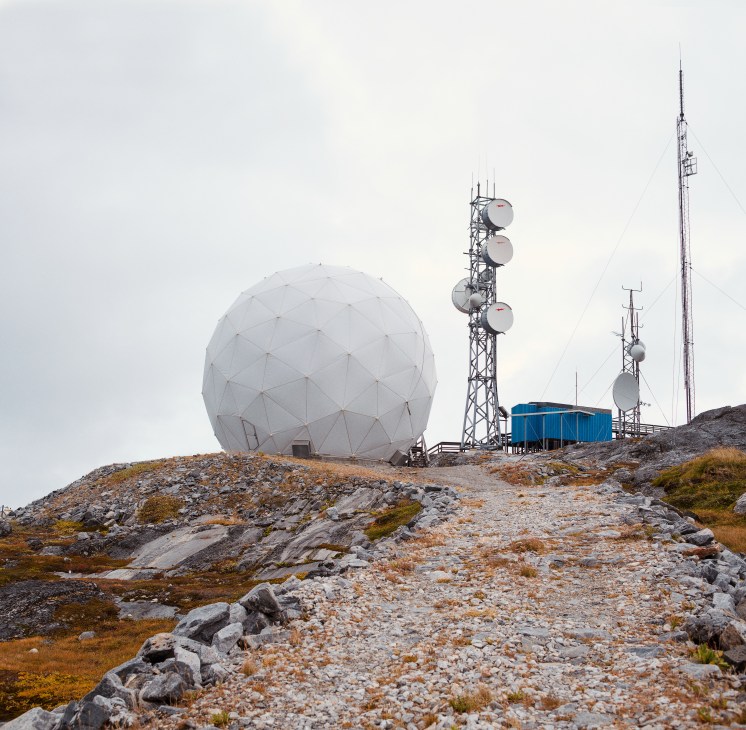 A white geodesic dome and telecommunications masts stand on a rocky Greenlandic hillside.
