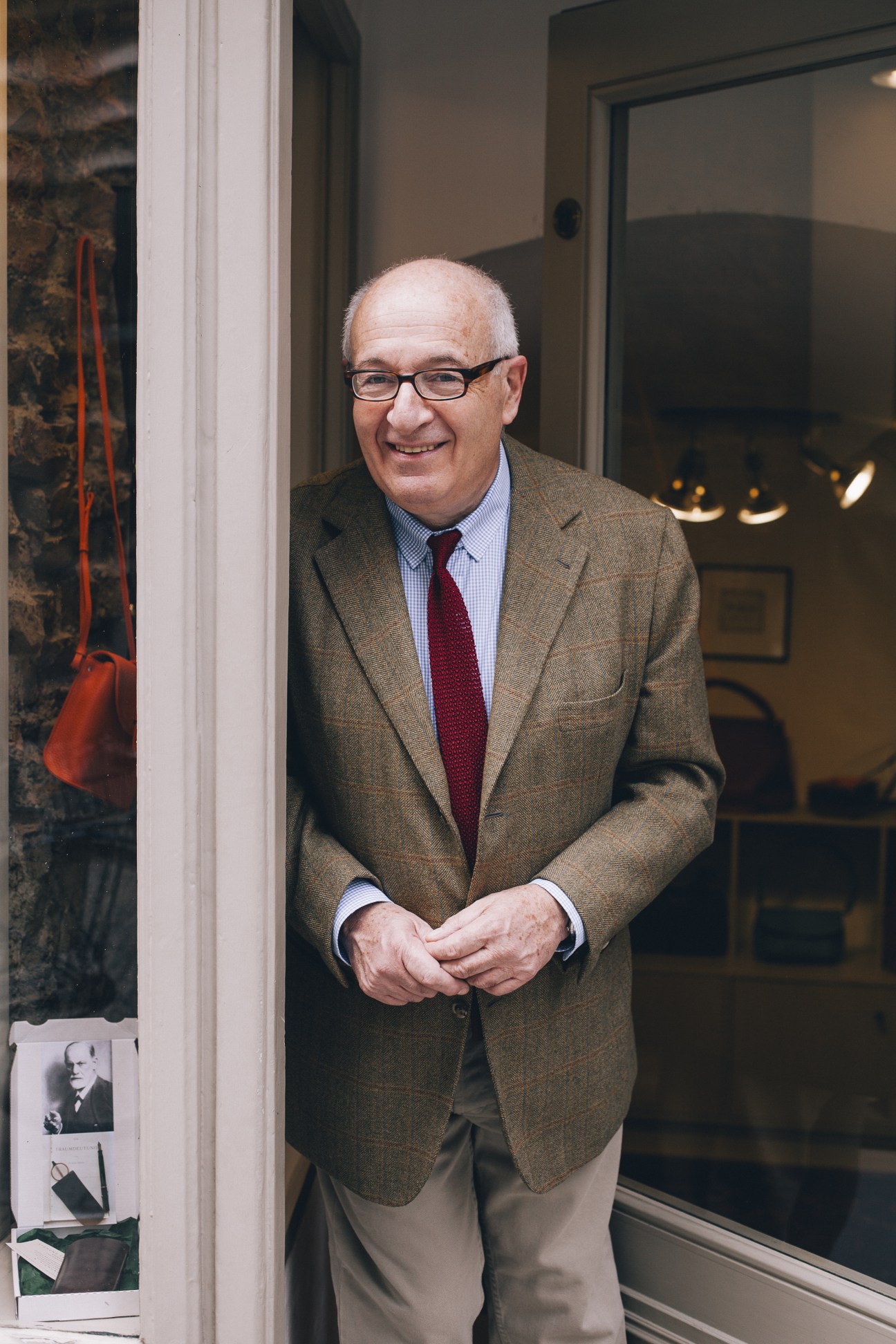 Man in glasses and brown blazer standing in doorway of R Horn leather goods shop.
