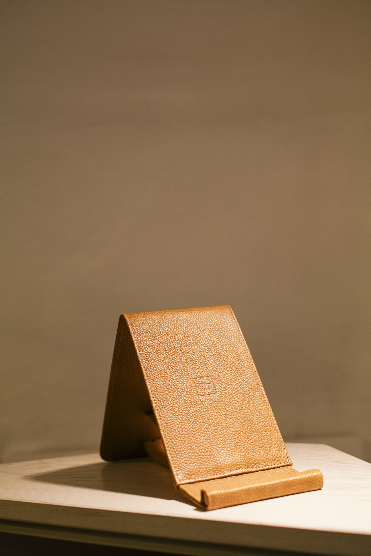 Tan leather wallet or card holder displayed on a wooden stand against a neutral background.