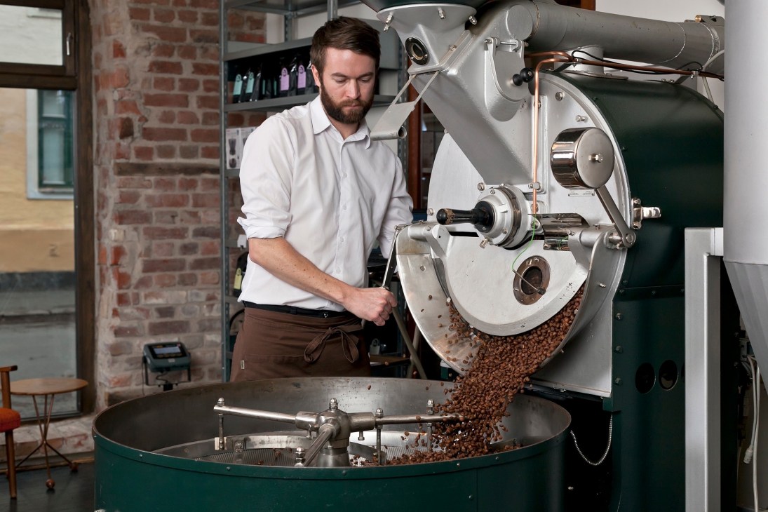 Tim Wendelboe operates a coffee roaster, pouring roasted beans into a cooling drum at his Oslo café.