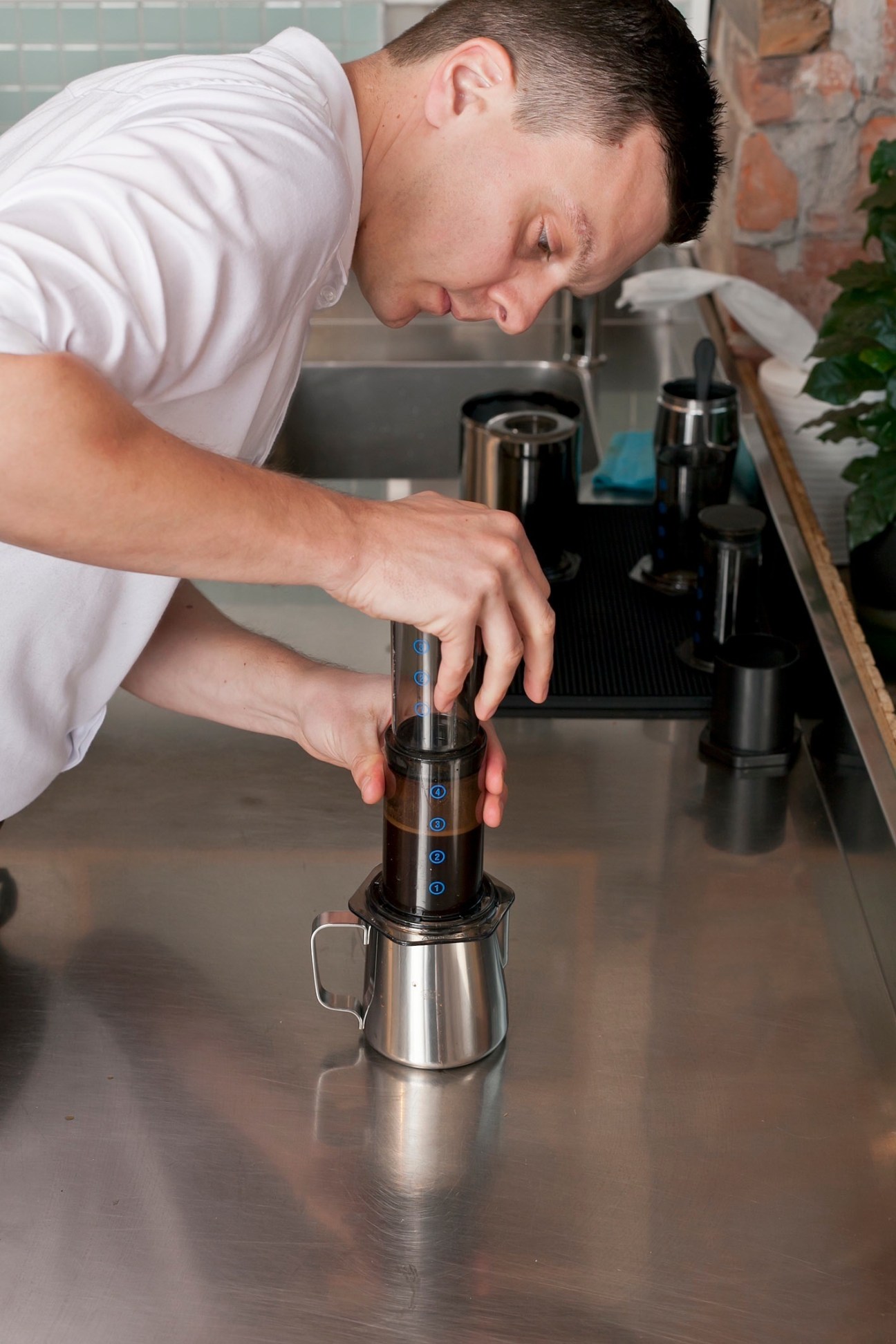 Man in white shirt operating a coffee grinder or brewing equipment at a counter.