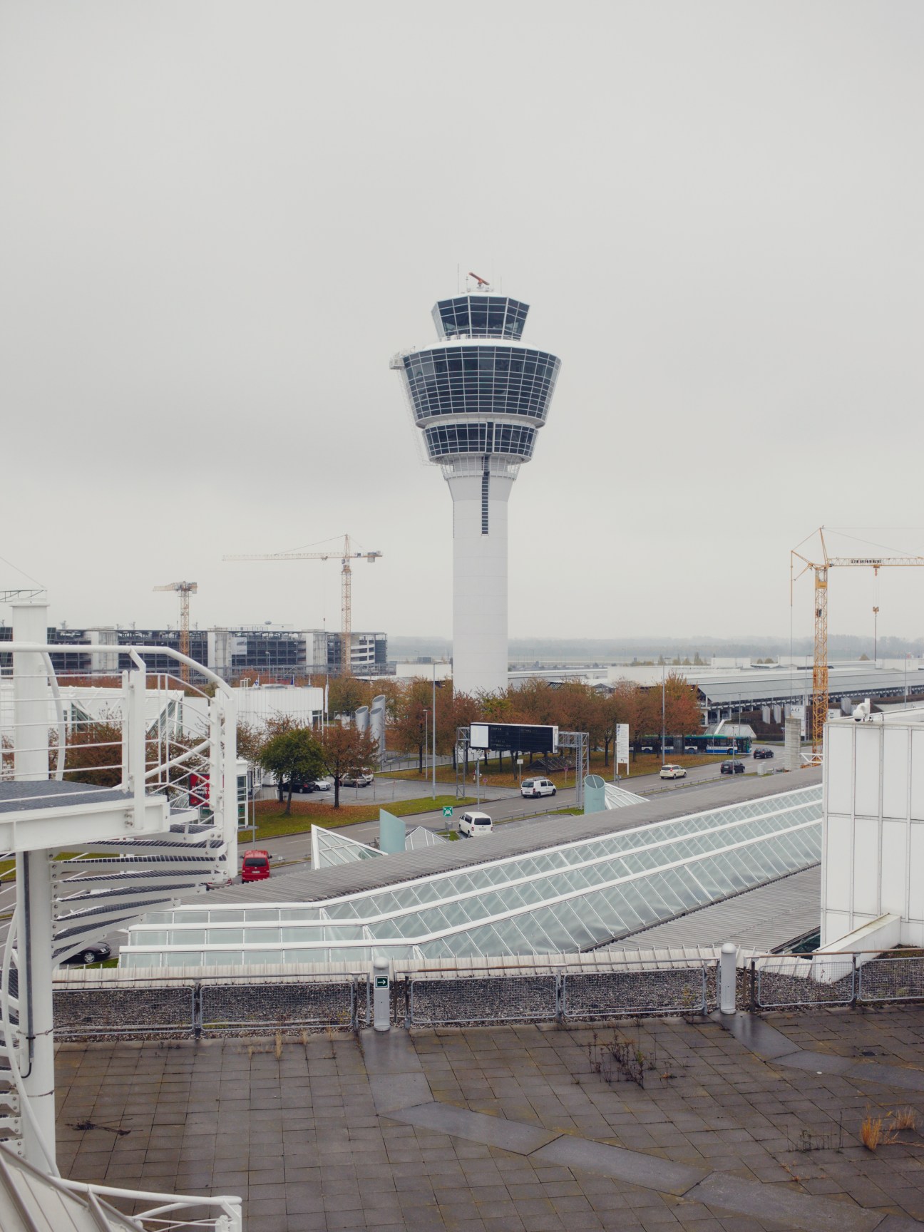 Munich airport control tower with solar panels and construction cranes in background.