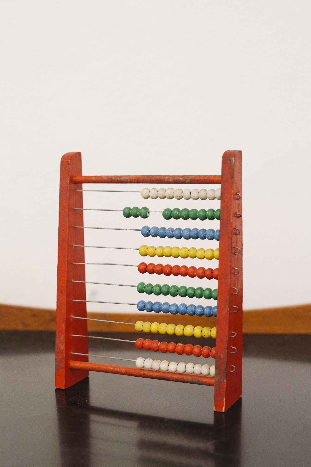 Vintage red wooden abacus with colorful beads on metal rods against neutral background.