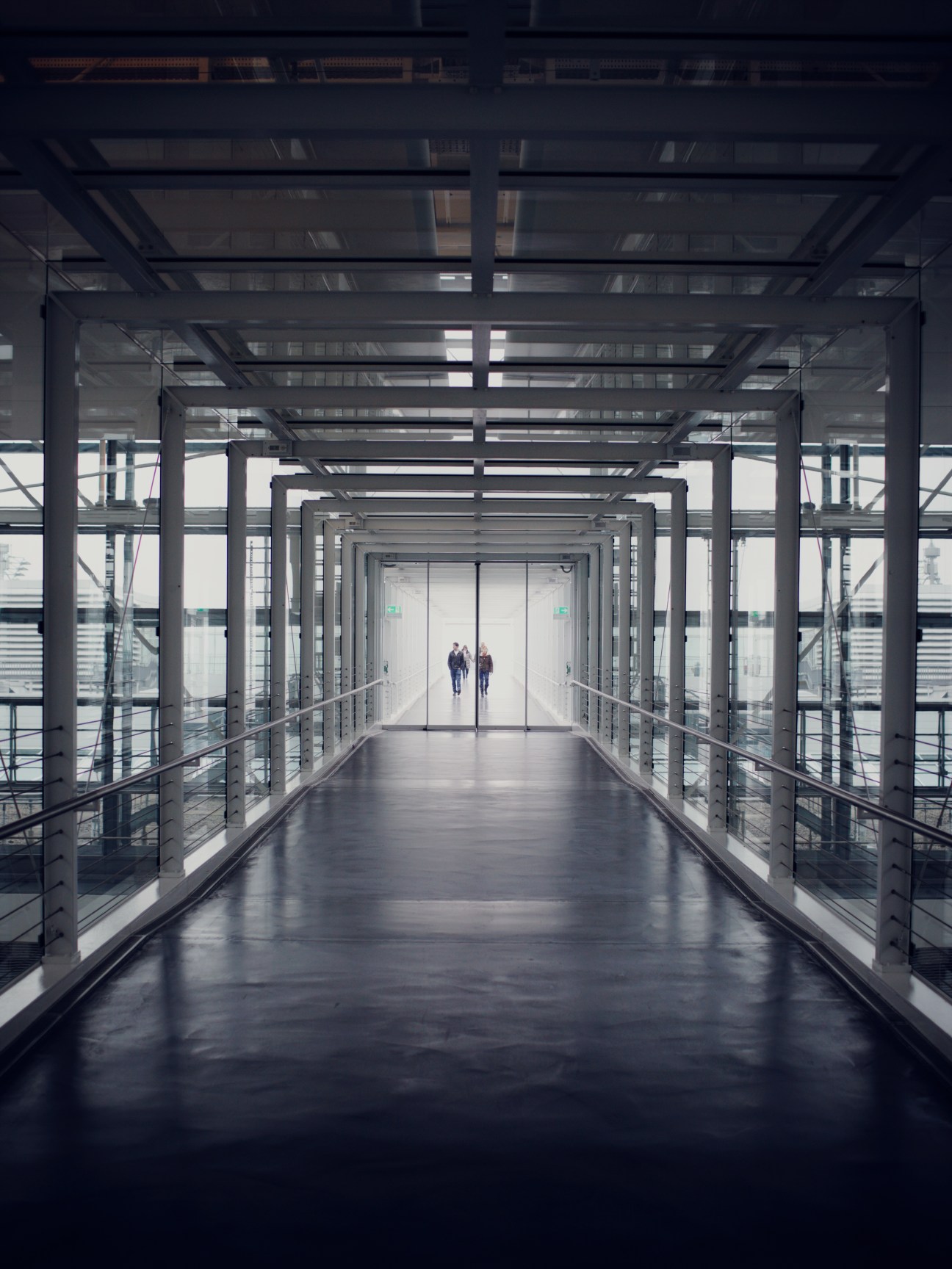 Modern airport corridor with steel framework, glass panels and geometric ceiling design.