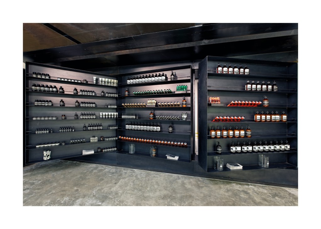 Black shelving display wall stocked with cosmetic and skincare products in glass jars and bottles.