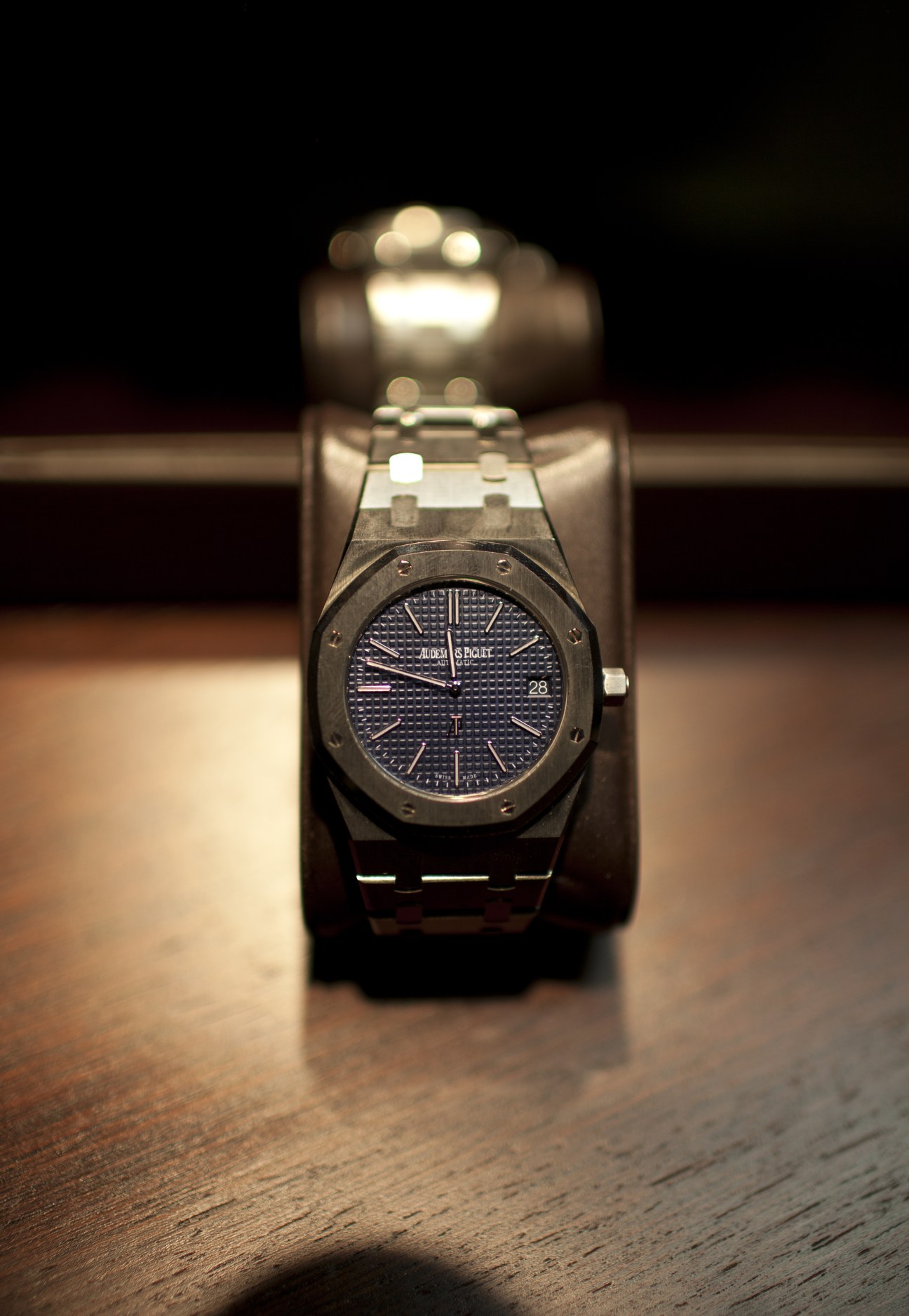 Audemars Piguet Extra-thin Royal Oak luxury stainless steel wristwatch on wooden surface with spotlit display.