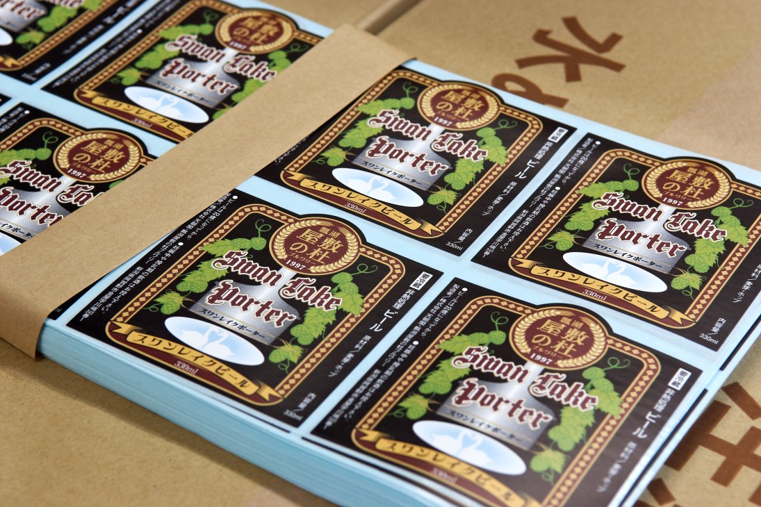 Multiple Swan Lake porter beer bottles with ornate gold and black labels featuring hop designs arranged on kraft paper.