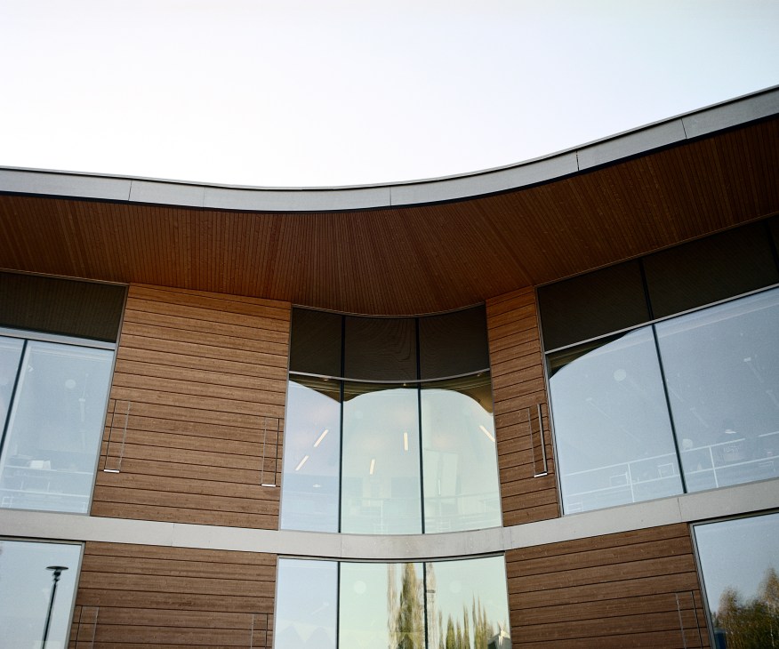 Curved exterior of Kirkkojärvi School with wood cladding and large glass windows.