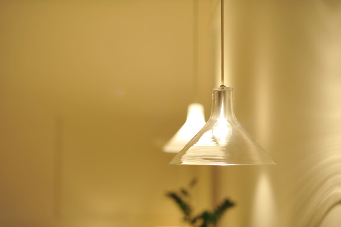 A brass pendant light by Flame designer Kenichi Kandatsu hanging against a warm yellow wall.