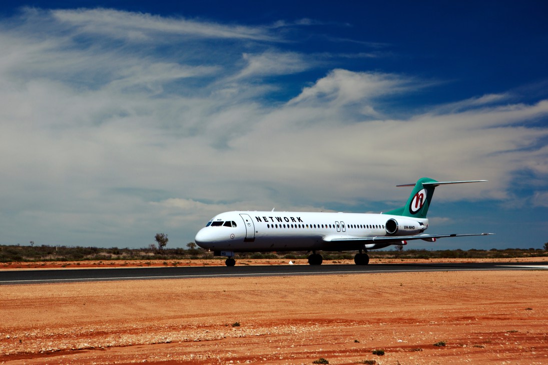 Network airline plane lands on red earth runway at Woodie Woodie mining camp in remote Australian Pilbara.