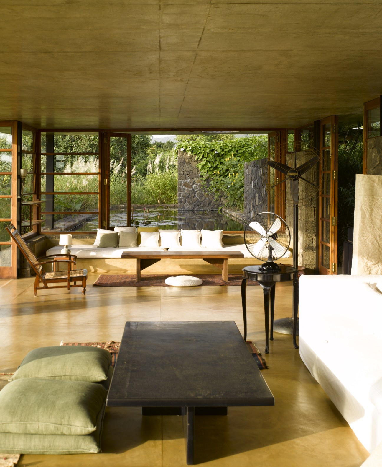 Modern living room with wooden furniture, large windows opening onto a pool and green landscape beyond.