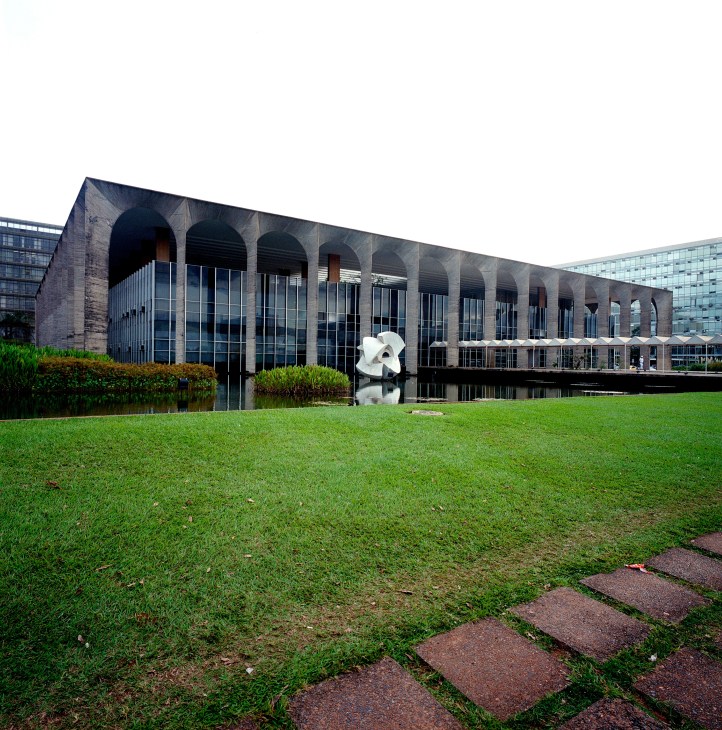 Modernist building with arched colonnade and reflecting pool, featuring white marble sculpture in garden setting.