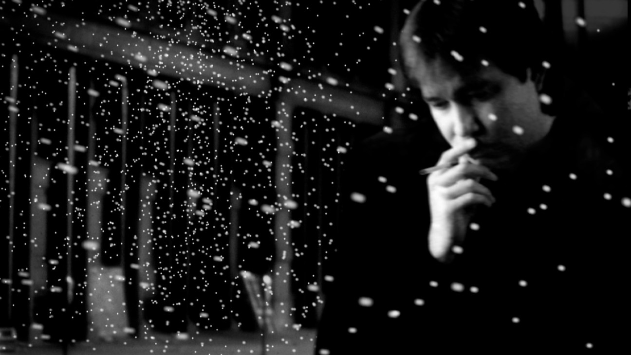Black and white still from American: The Bill Hicks Story showing a man in profile smoking with atmospheric lighting effects.