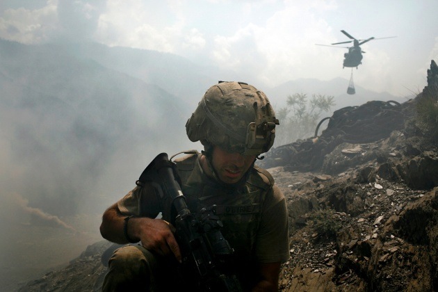 US soldier in combat gear on rocky terrain with military helicopter in background during Afghanistan deployment.