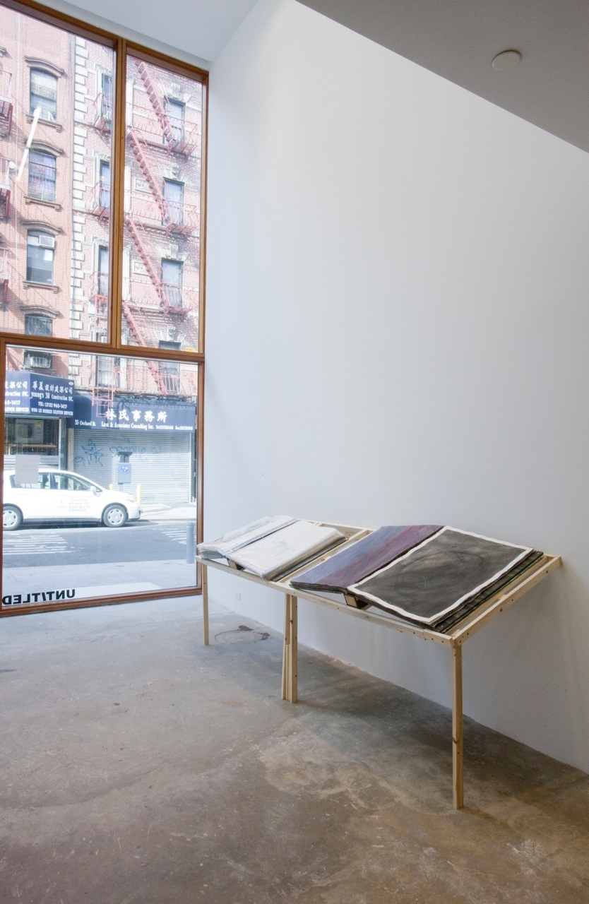 Interior of Untitled gallery showing wooden display table with fabric samples near storefront window.