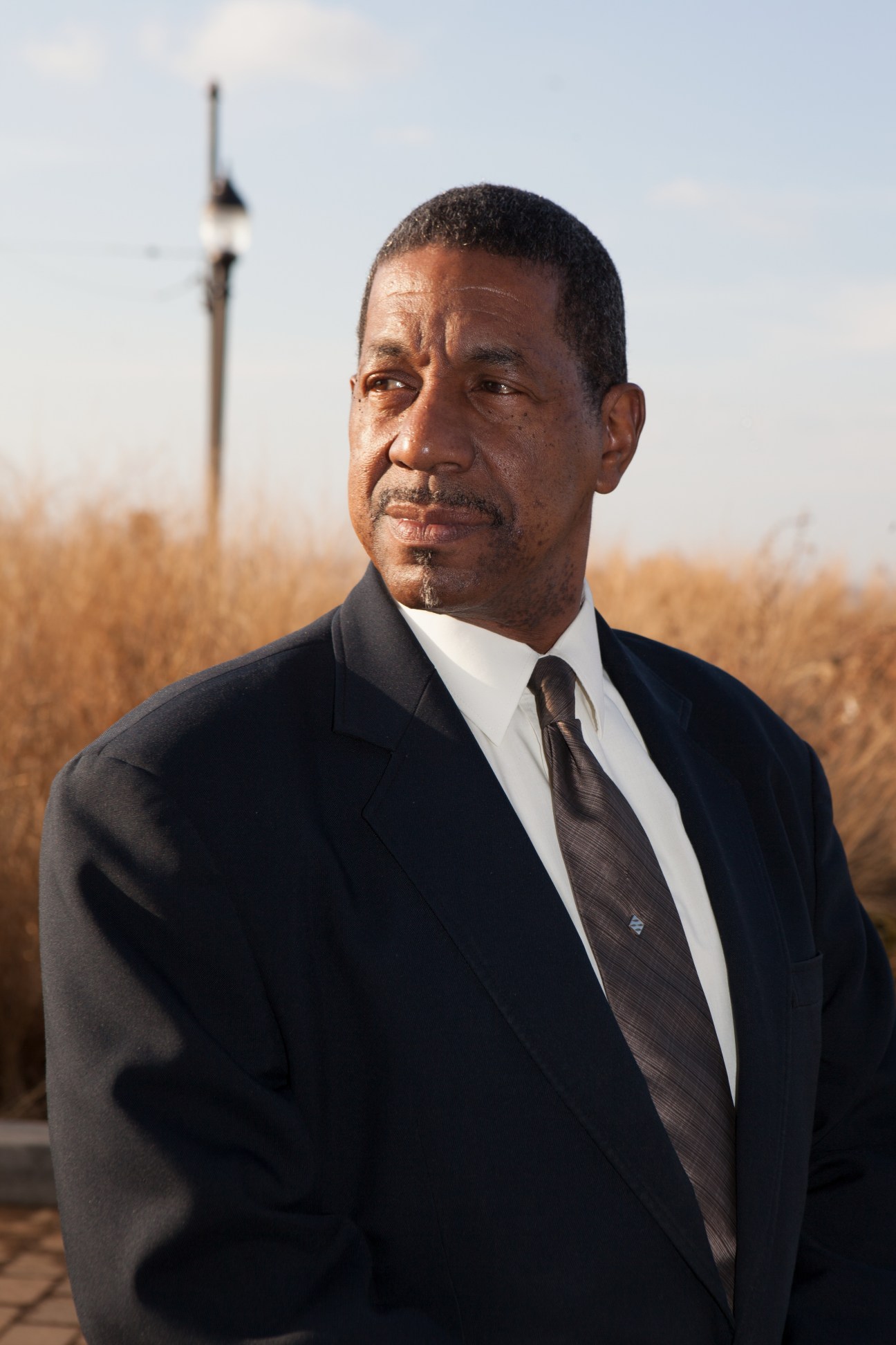 Hal Brown, doorman and community activist, wearing a dark suit and tie against an outdoor background with a flagpole.