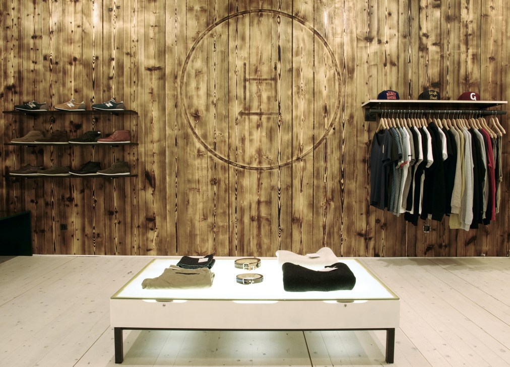 Interior of Harvest boutique in Munich showing wooden wall with shoe displays, circular mirror, clothing rack, and white display table.