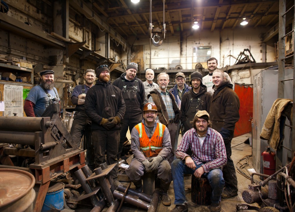 Group portrait of workers at Magone Marine salvage company in an industrial workshop setting.