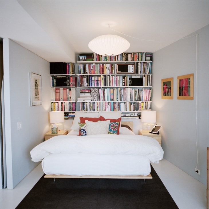 Modern bedroom with built-in shelving above light wood bed frame and white bedding