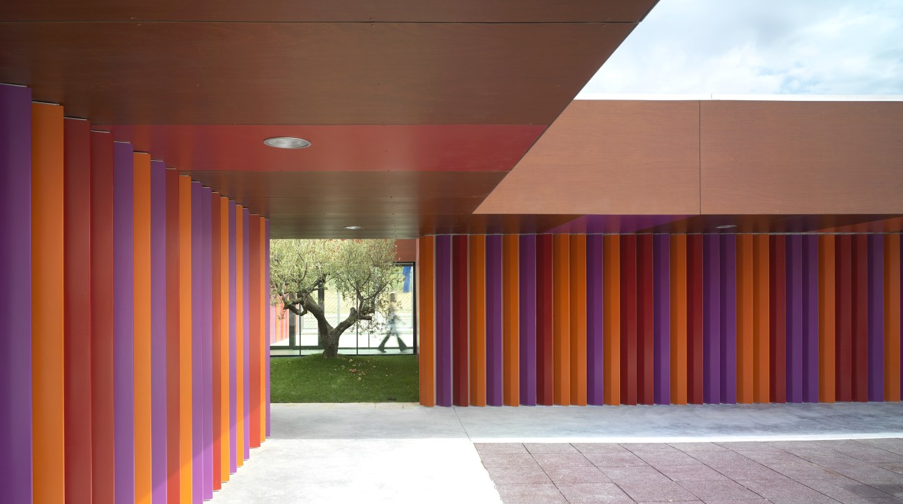 Colorful interior corridor of a kindergarten with vibrant purple, orange and red vertical boards lining the walls and skylights overhead.