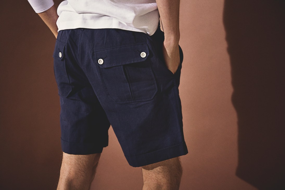 Man wearing navy Japanese gabardine camping shorts with button-flap pockets and white shirt.