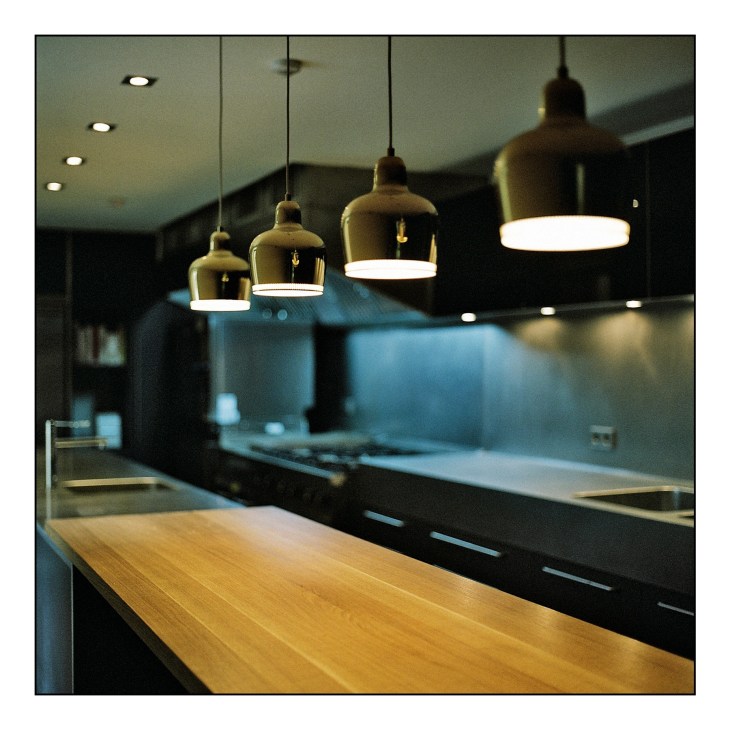 Modern kitchen with wooden counter and black cabinetry beneath pendant lights.