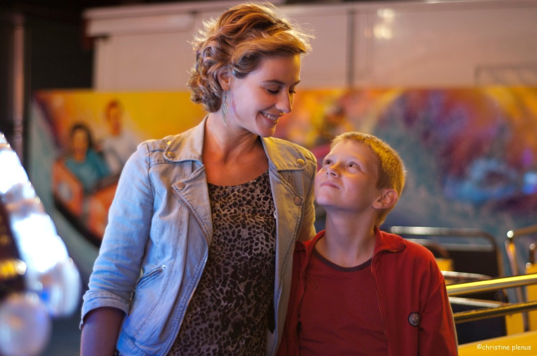 Woman and young boy smile together in a colorful indoor setting with yellow background.
