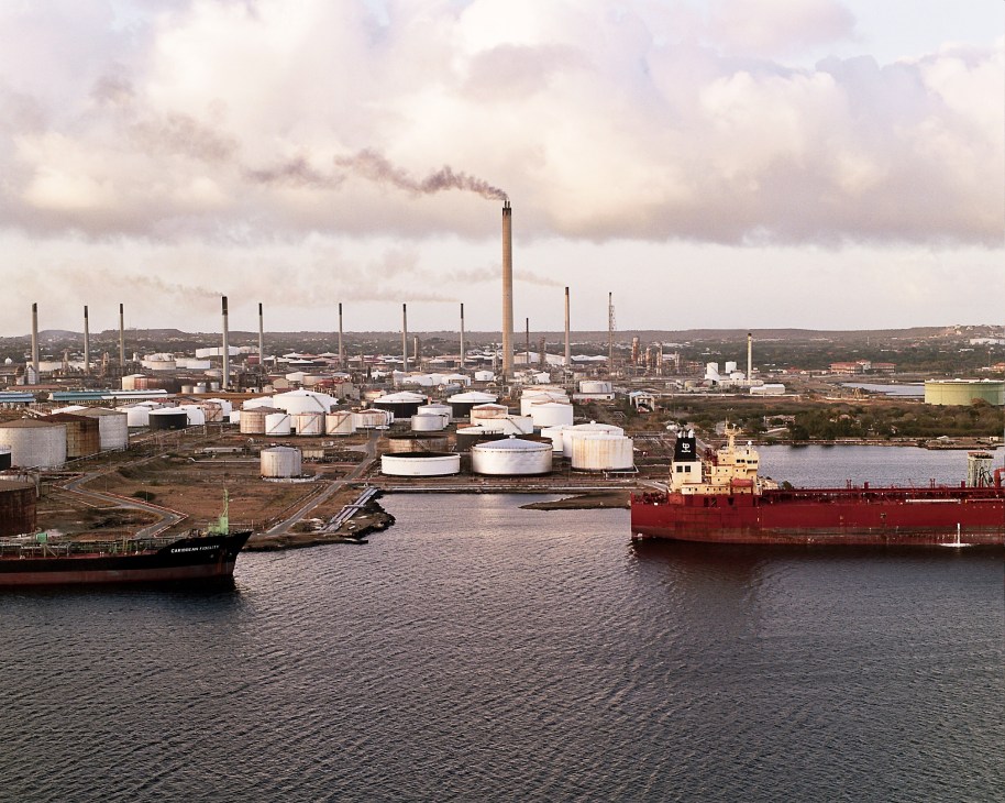 Oil refinery and port in Willemstad with storage tanks, smokestacks, and cargo ships docked in the harbor.