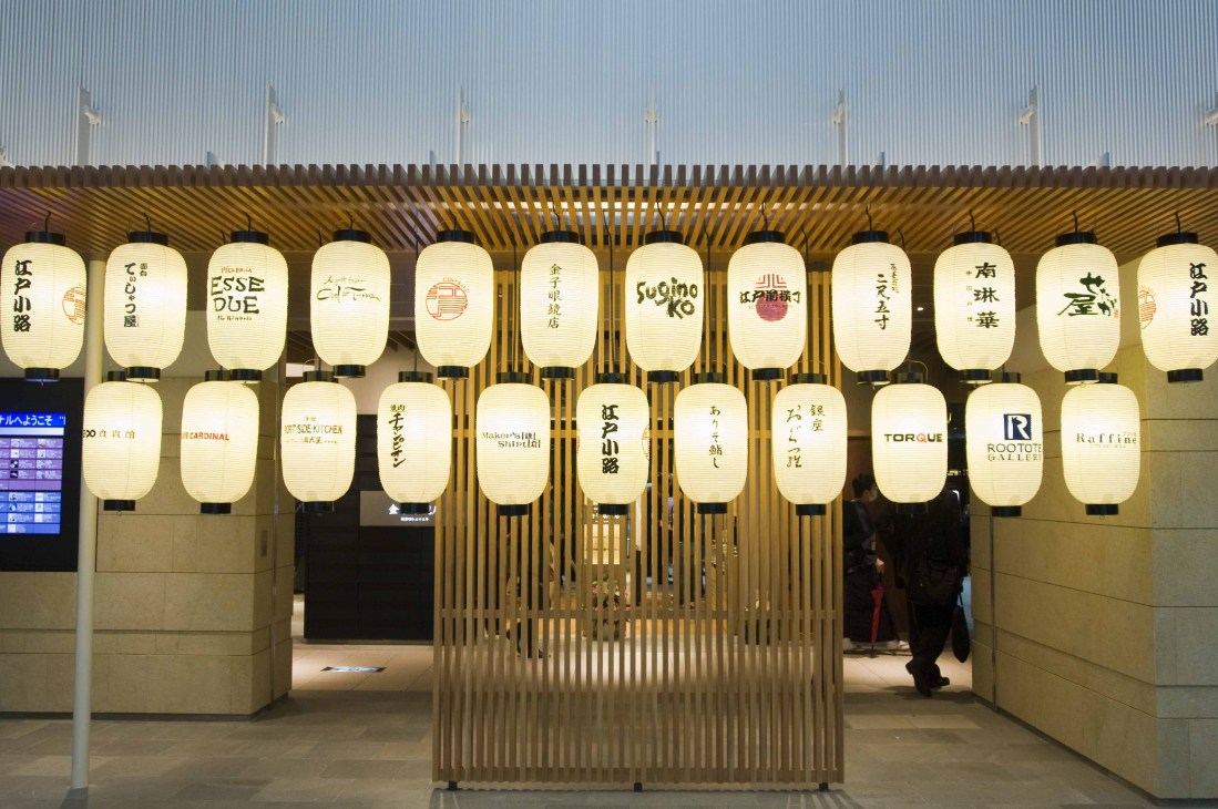 Edo-period inspired shopping village at Tokyo Haneda airport with cream paper lanterns displaying Japanese characters and restaurant names.