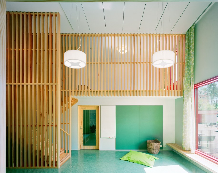 Interior of Finnish daycare centre with timber-slatted walls, green colour accents, pendant lights and natural fibre storage.