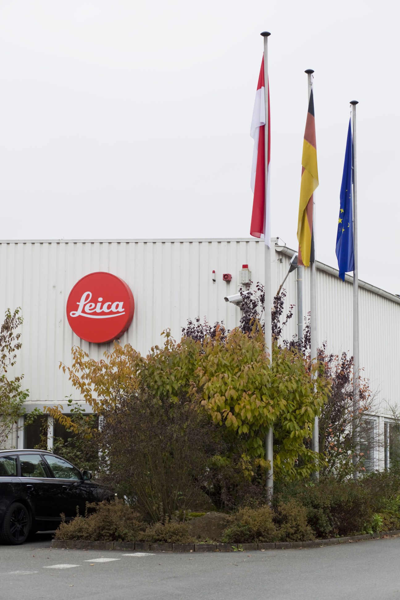 Leica factory building exterior with red circular logo and international flags on poles.
