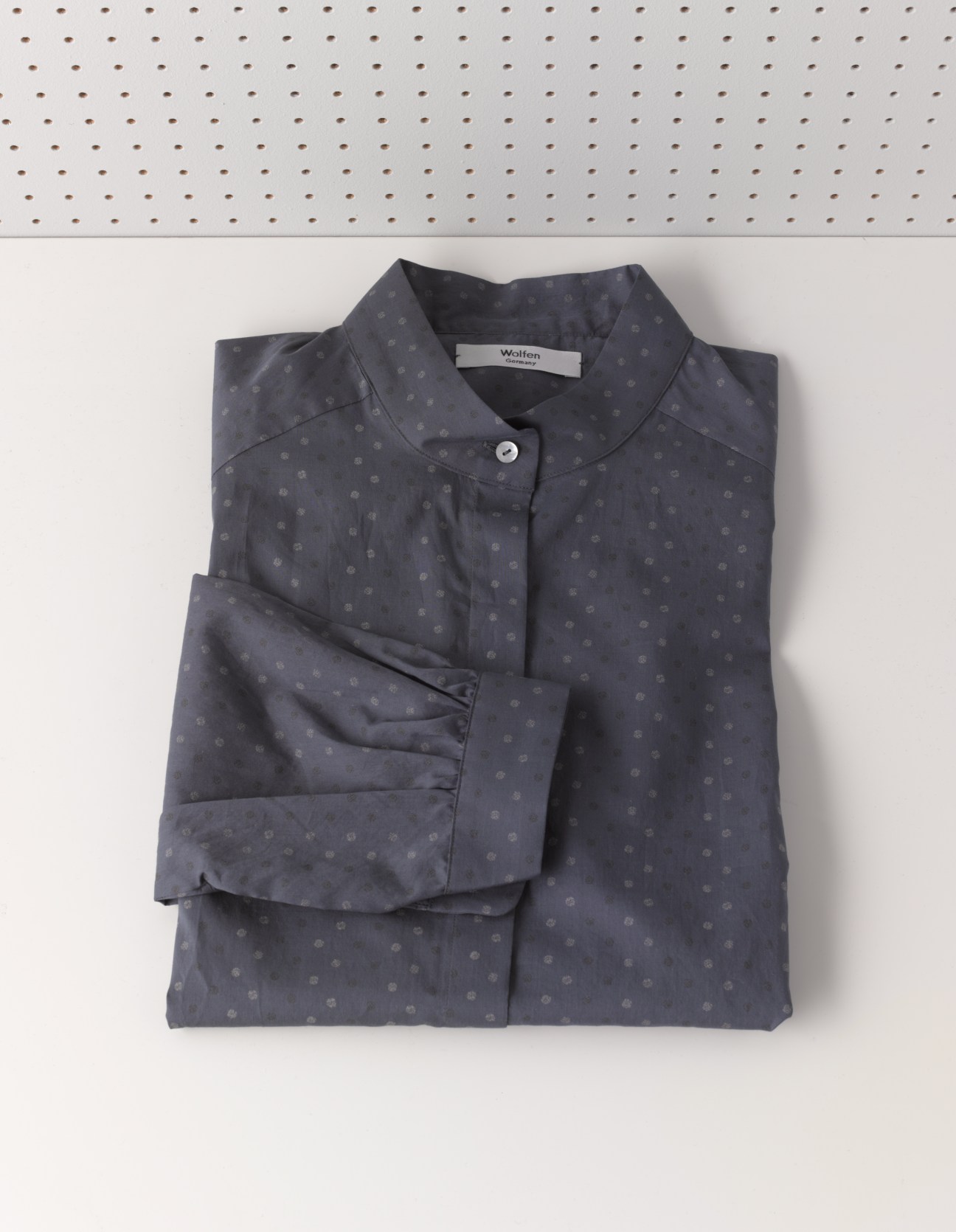 Wolfen navy button-up shirt with subtle dot pattern, folded on white pegboard background.