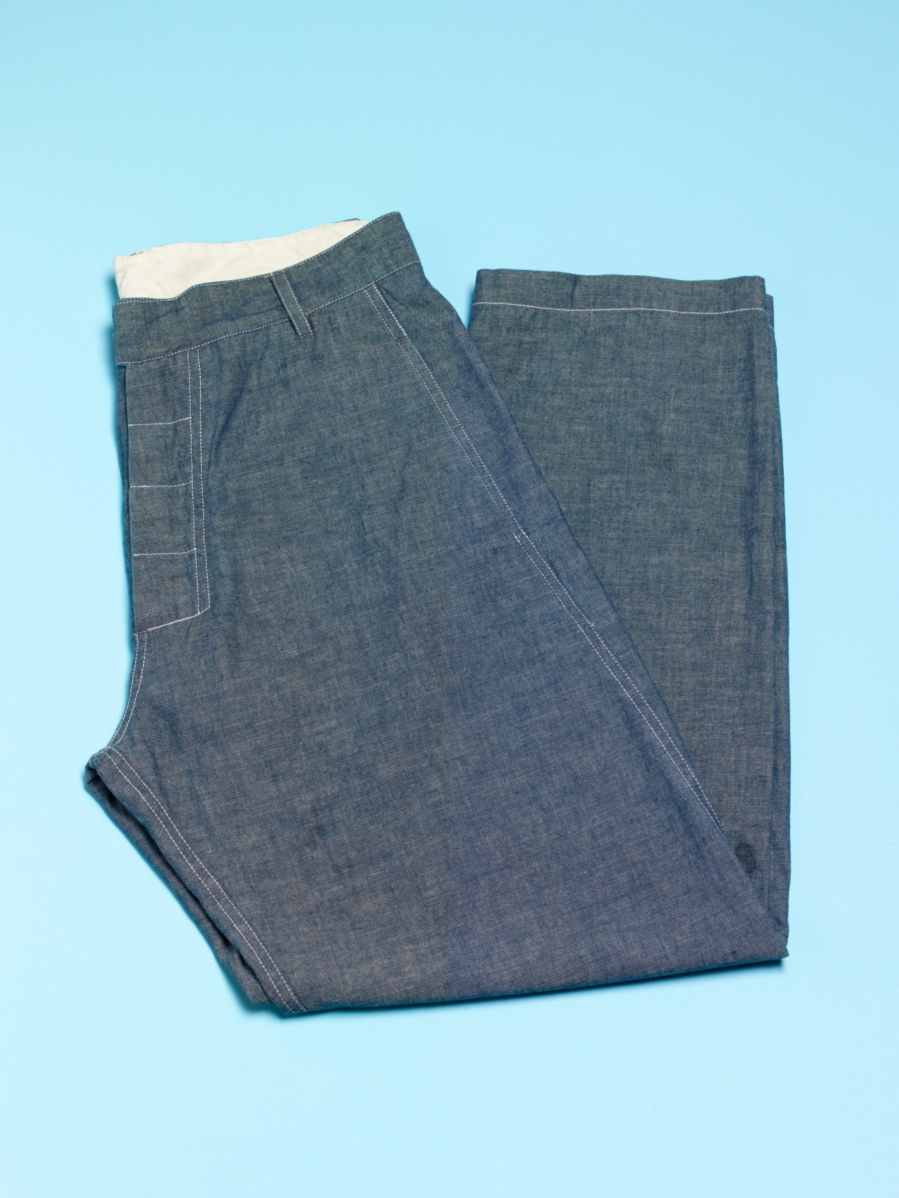 Folded blue denim jeans with white waistband against light blue background.