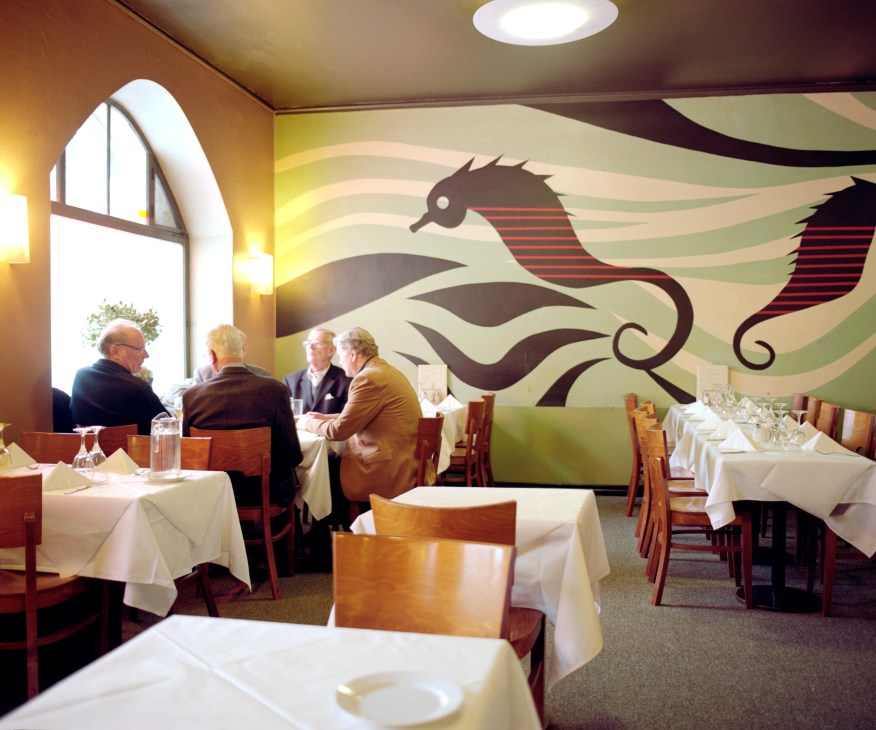 Interior of Restaurant Sea Horse with diners at white-clothed tables and stylized seahorse mural on wall.
