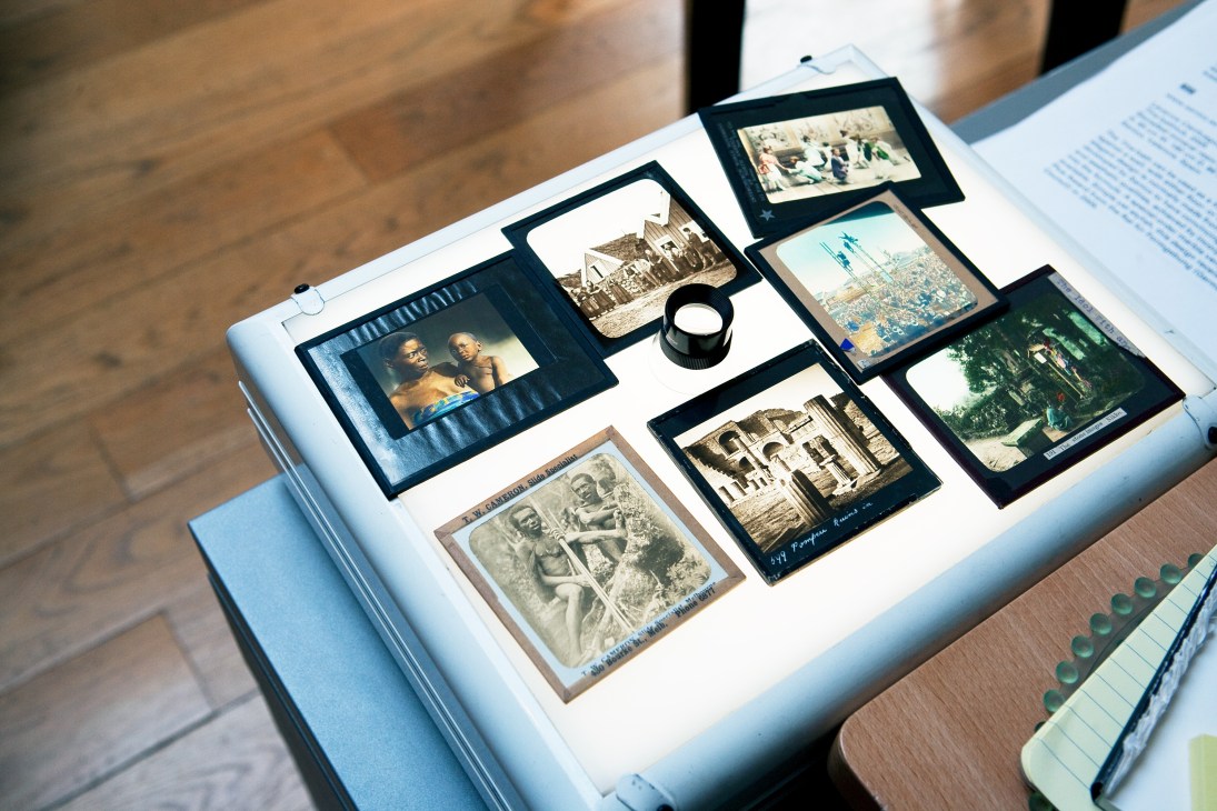 Collection of vintage magic lantern slides displayed on a white surface with a magnifying glass.