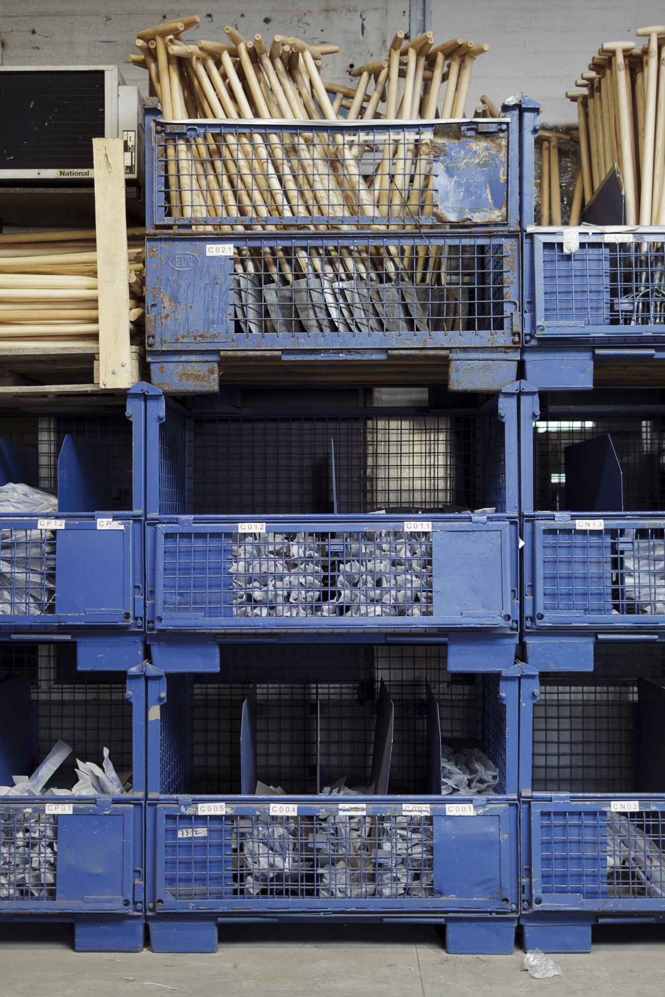 Wooden-handled garden tools stacked in blue metal cages awaiting dispatch at DeWit factory.
