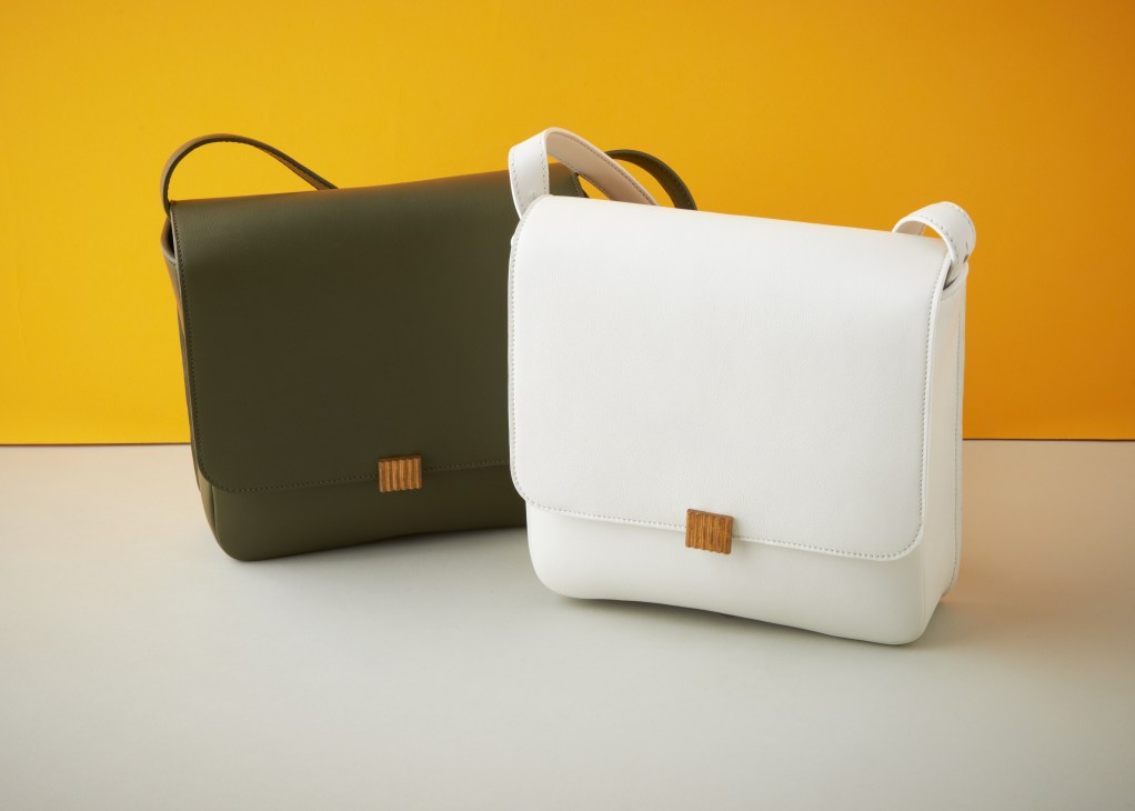 Two leather shoulder bags in olive green and white with wooden detail hardware against a yellow and beige background.