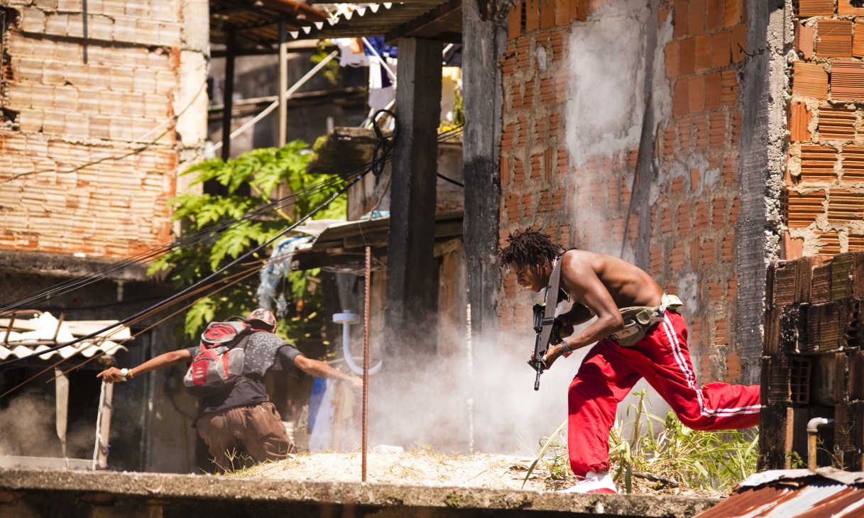 Scene from Elite Squad II showing actors in a favela setting with gunfire and dust effects.