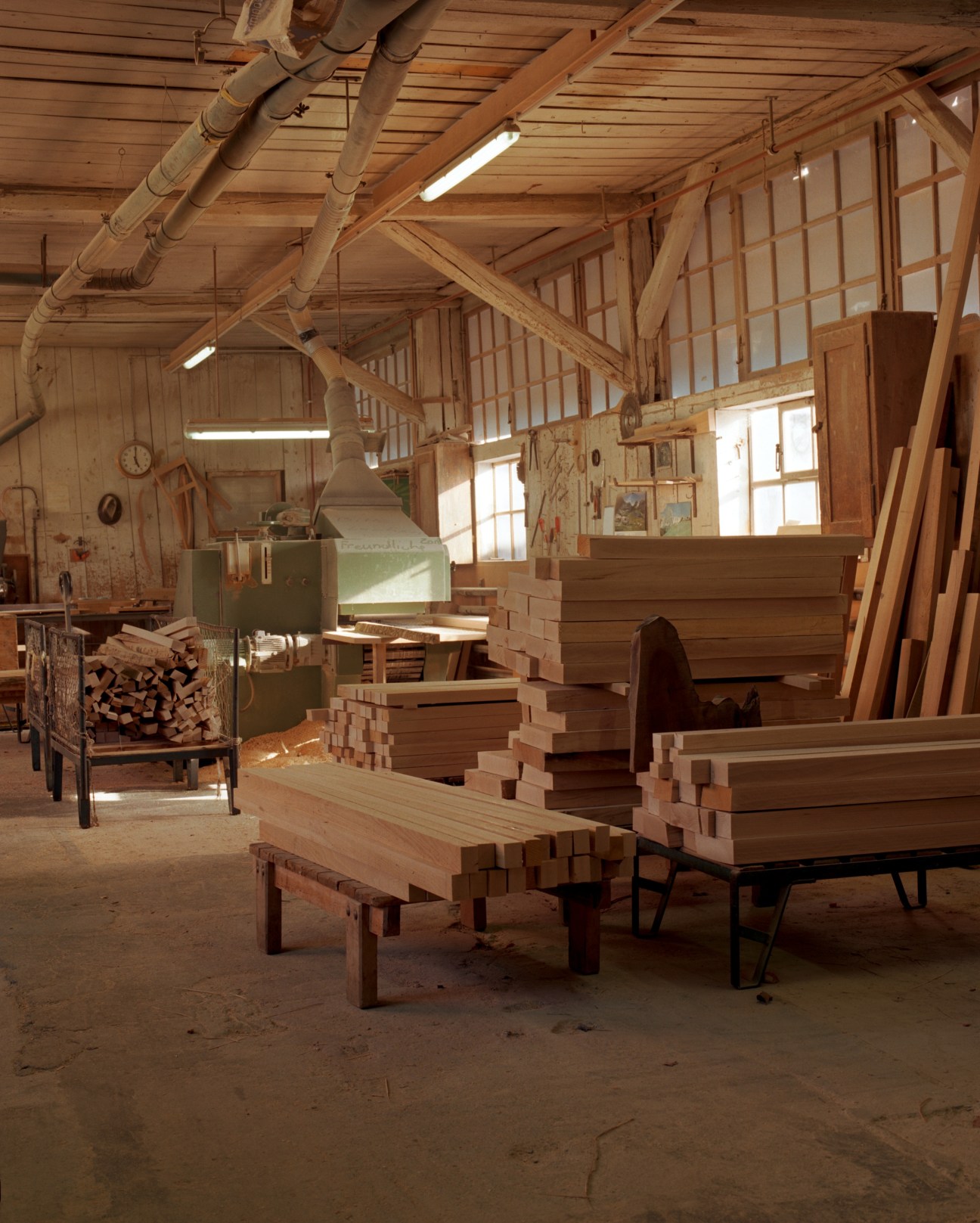 Wooden planks stacked in Horgenglarus mill workshop with exposed beam ceiling and industrial lighting.