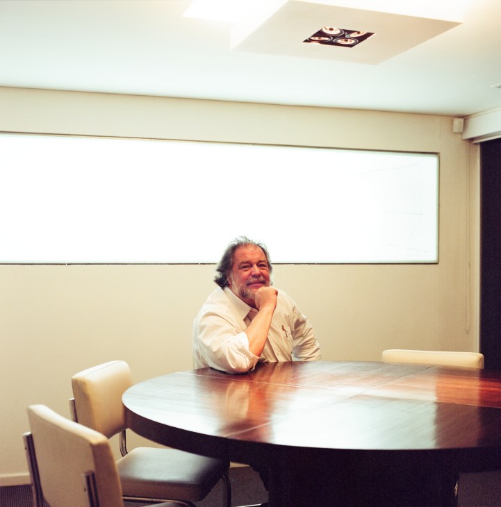 Architect Gustavo Penna sits at a round table in his modern office with a whiteboard behind him.