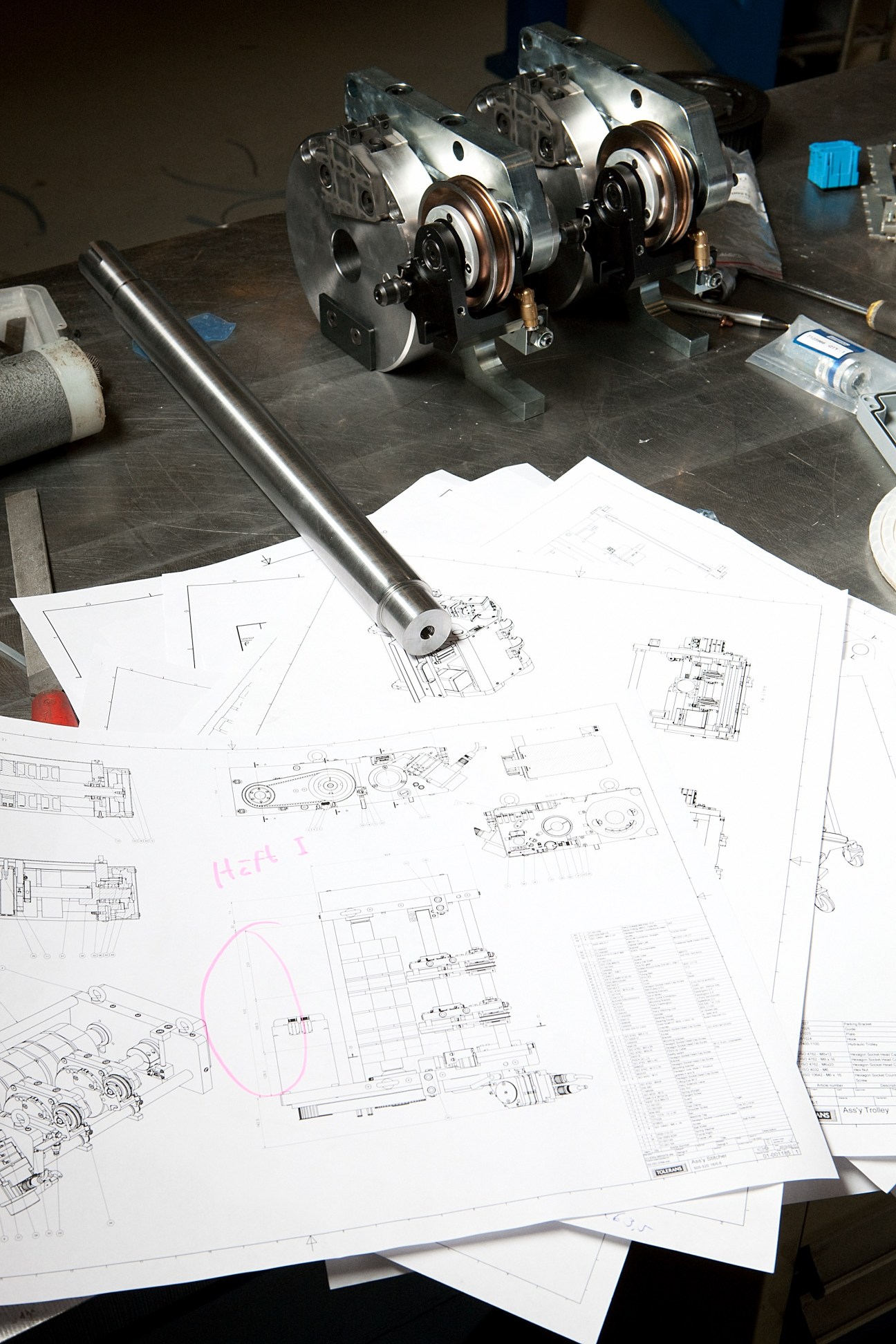 Technical design blueprints and mechanical parts laid on a workbench at Tolerans factory.