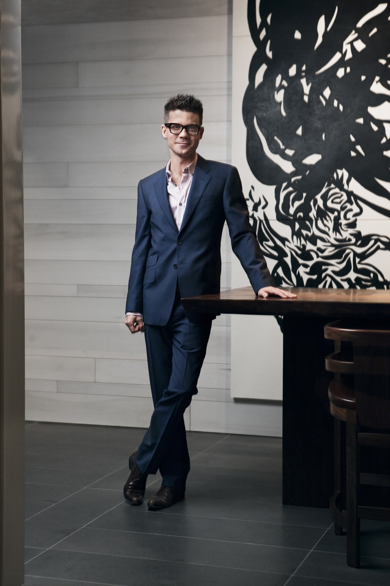 General manager Jonathan Frolich stands in a modern hotel corridor wearing a navy blazer and glasses.
