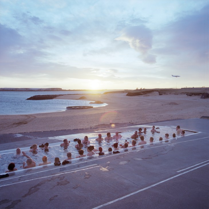 Bathers enjoy a geothermal pool at sunset overlooking an Icelandic beach and sea.