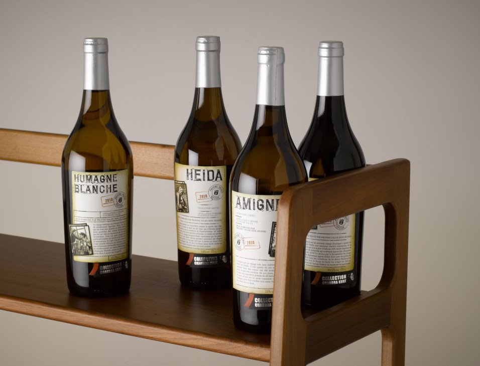 Four Swiss wine bottles in a wooden carrier, including Humagne Blanche, Heida, and Amigni varieties from Collection Chandra Kurt.