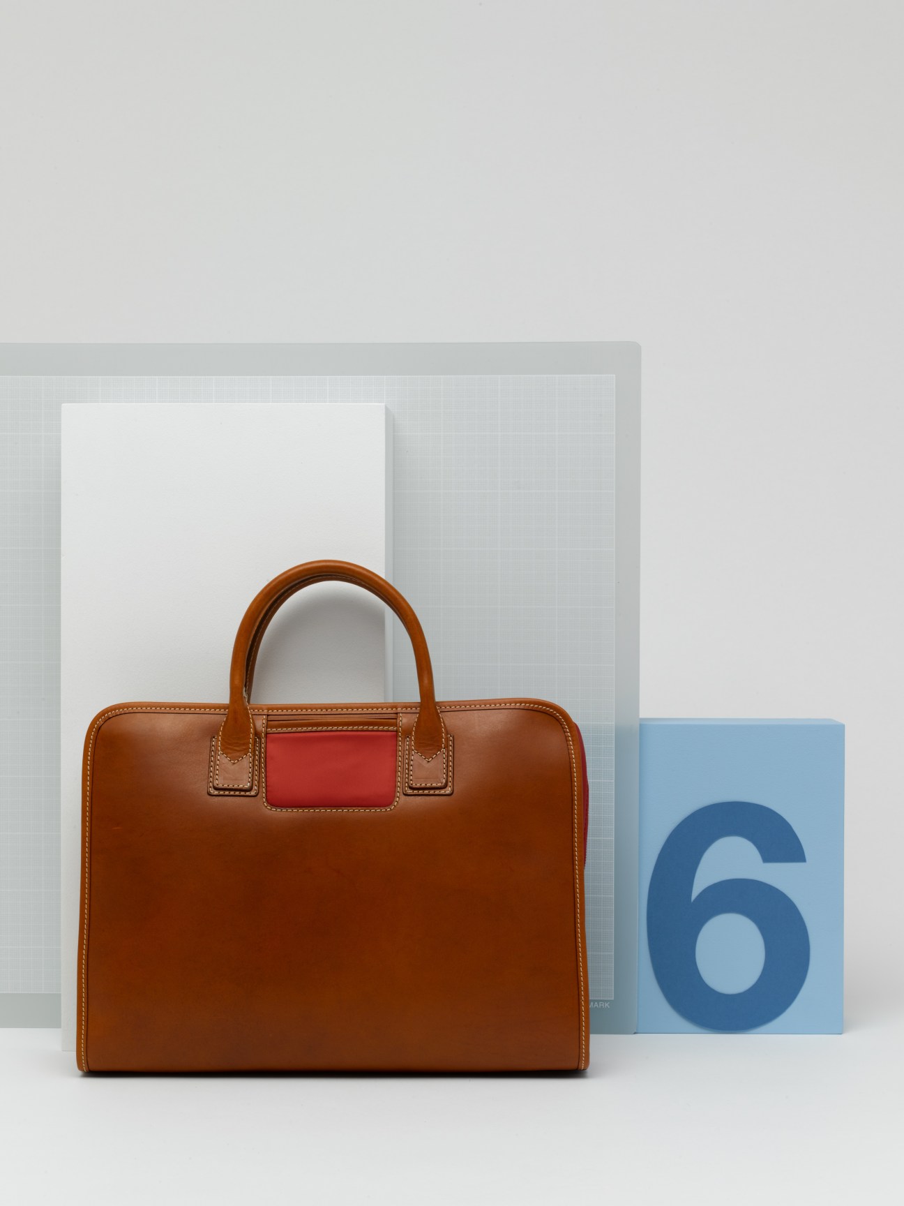 Brown leather Travelteq laptop bag with red accent panel and tan stitching displayed with design materials.